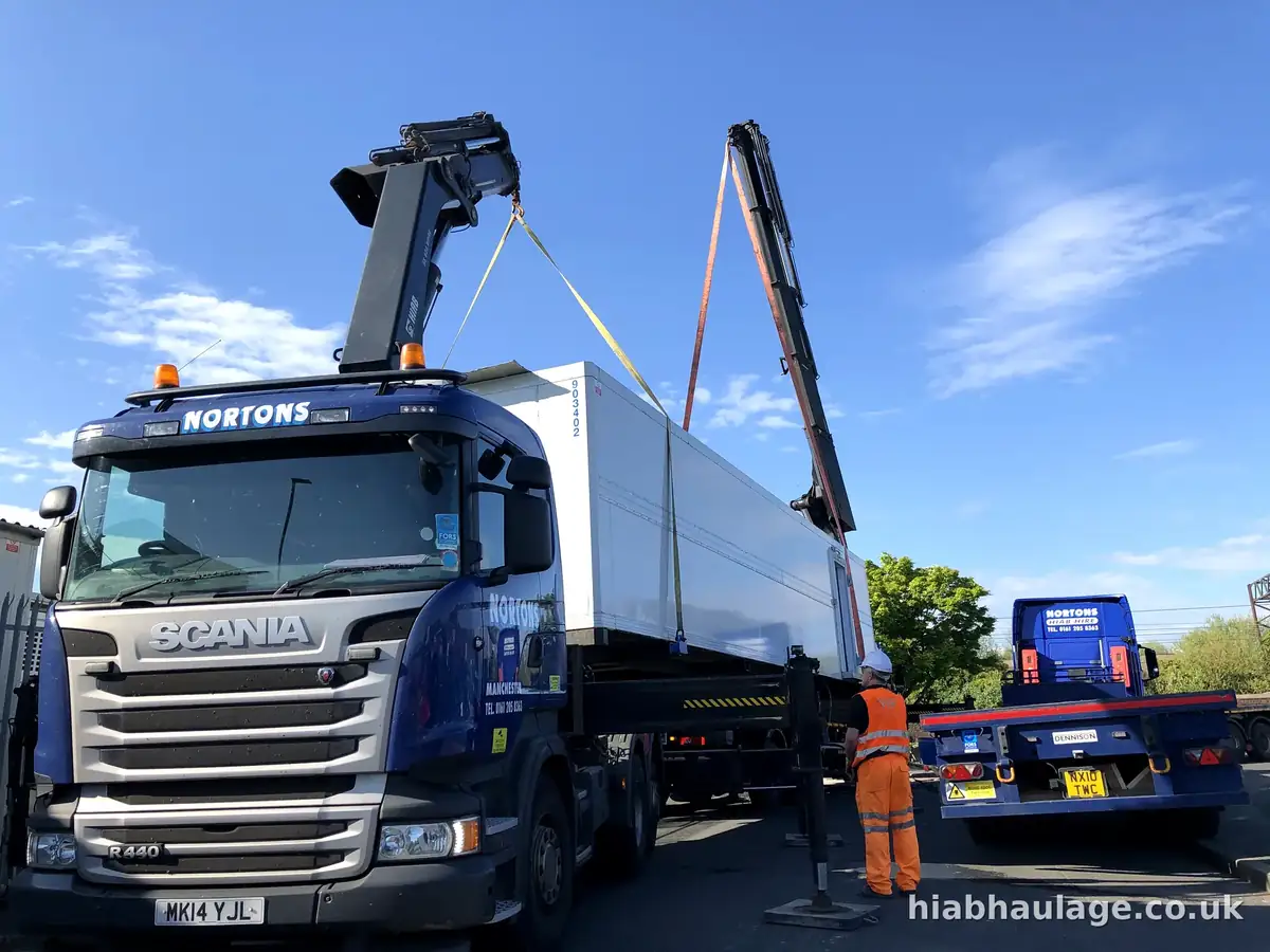 Two HIABs lifting a freezer unit from a trailer