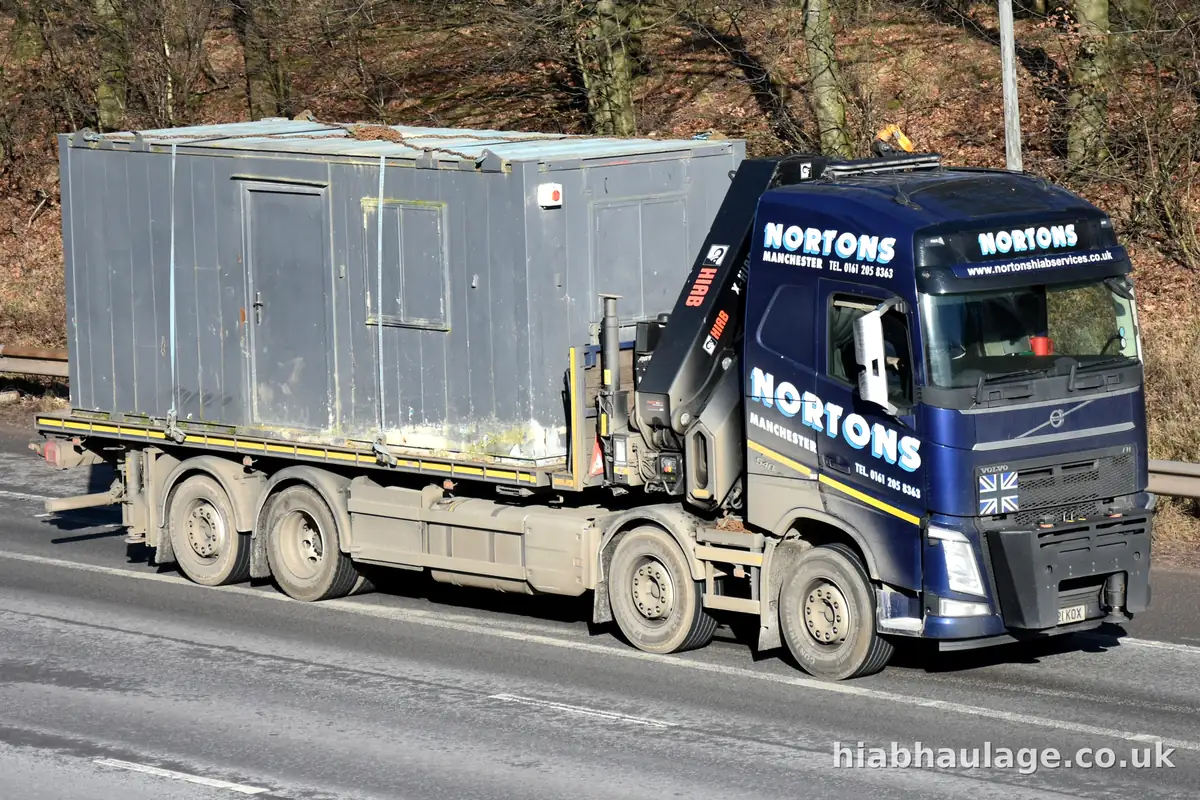 Rigid HIAB lorry carrying a grey site cabin along a dual carriageway