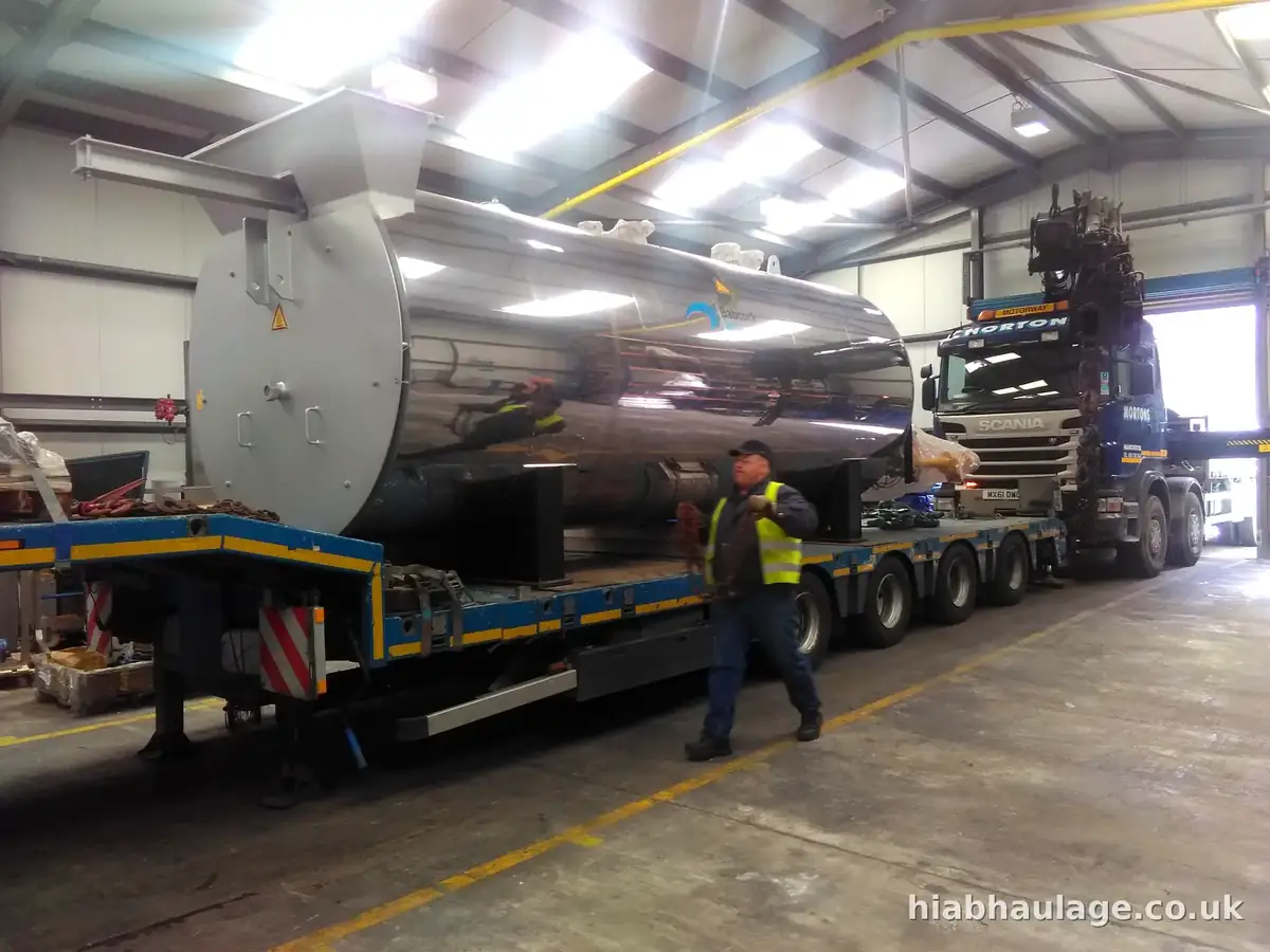 Large stainless boiler unit on a low loader inside a factory