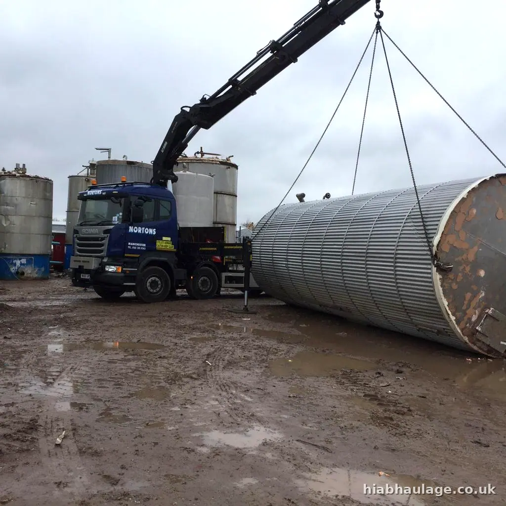 Rigid HIAB lifting a large ribbed steel tank in a muddy yard