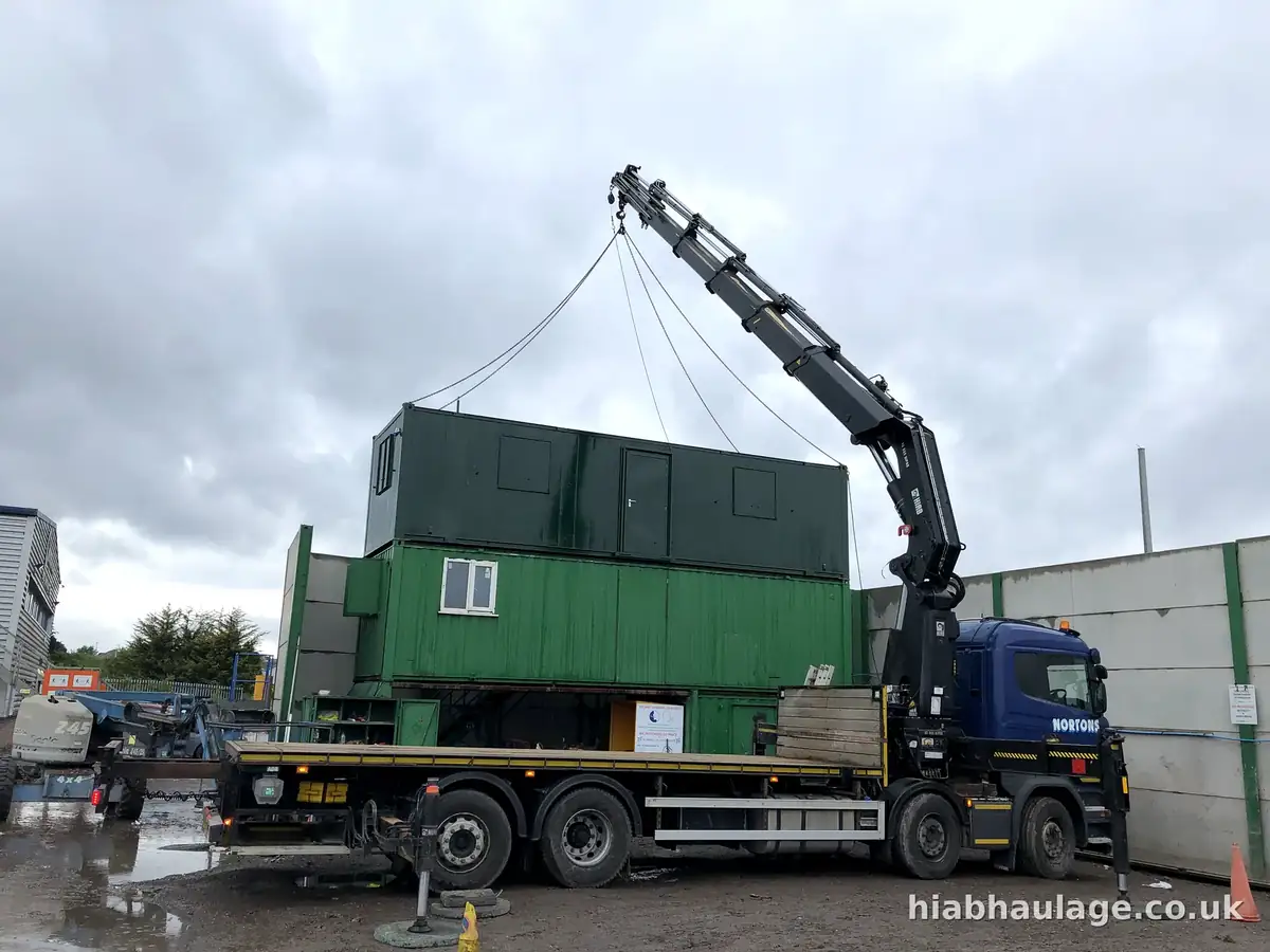 Rigid HIAB setting a cabin down onto a stack, side view