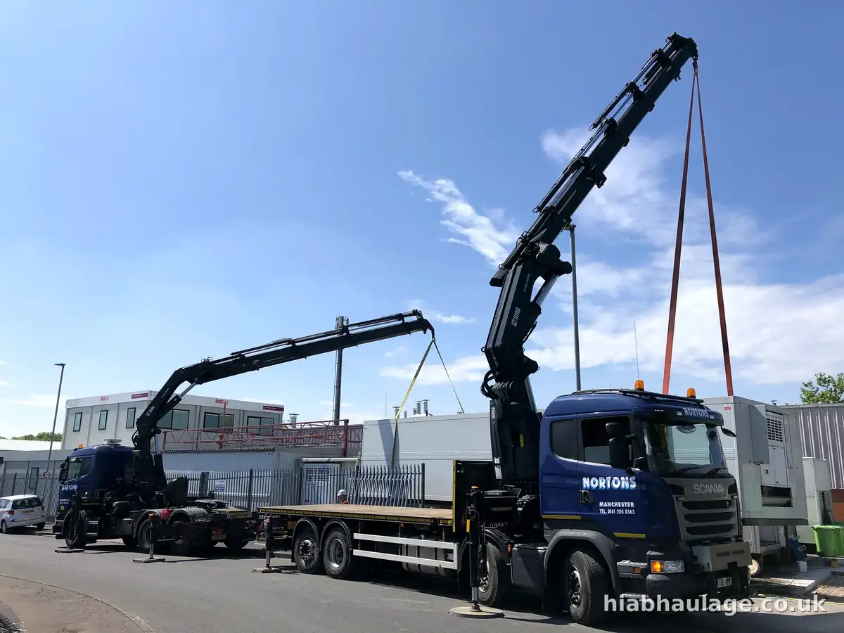 Two HIABs lifting together beside a row of cabins