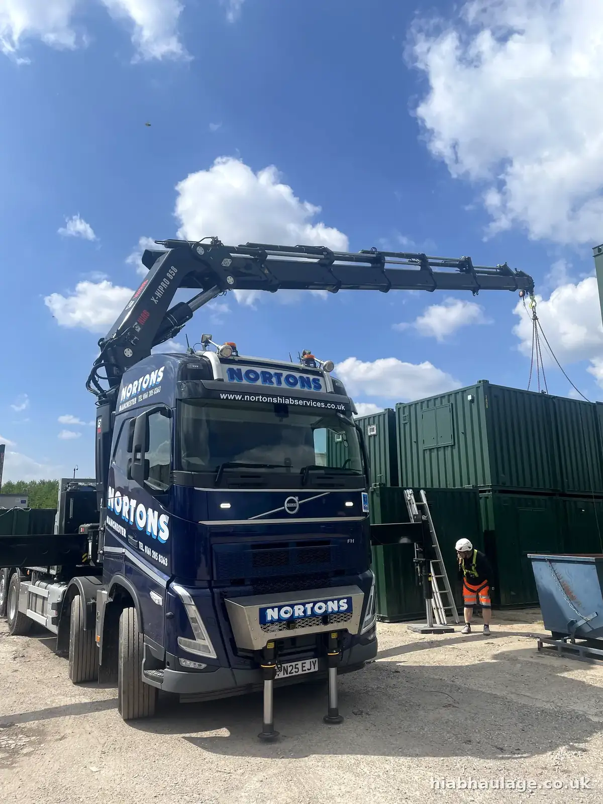 Volvo HIAB lifting in a yard beside green cabins Volvo HIAB lifting in a yard beside green cabins